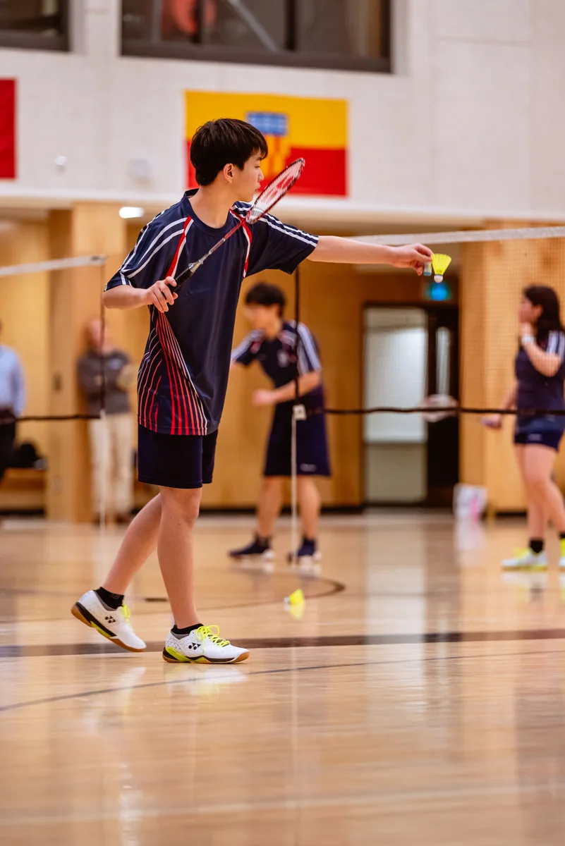 A badminton player reaching to hit the shuttle at the net