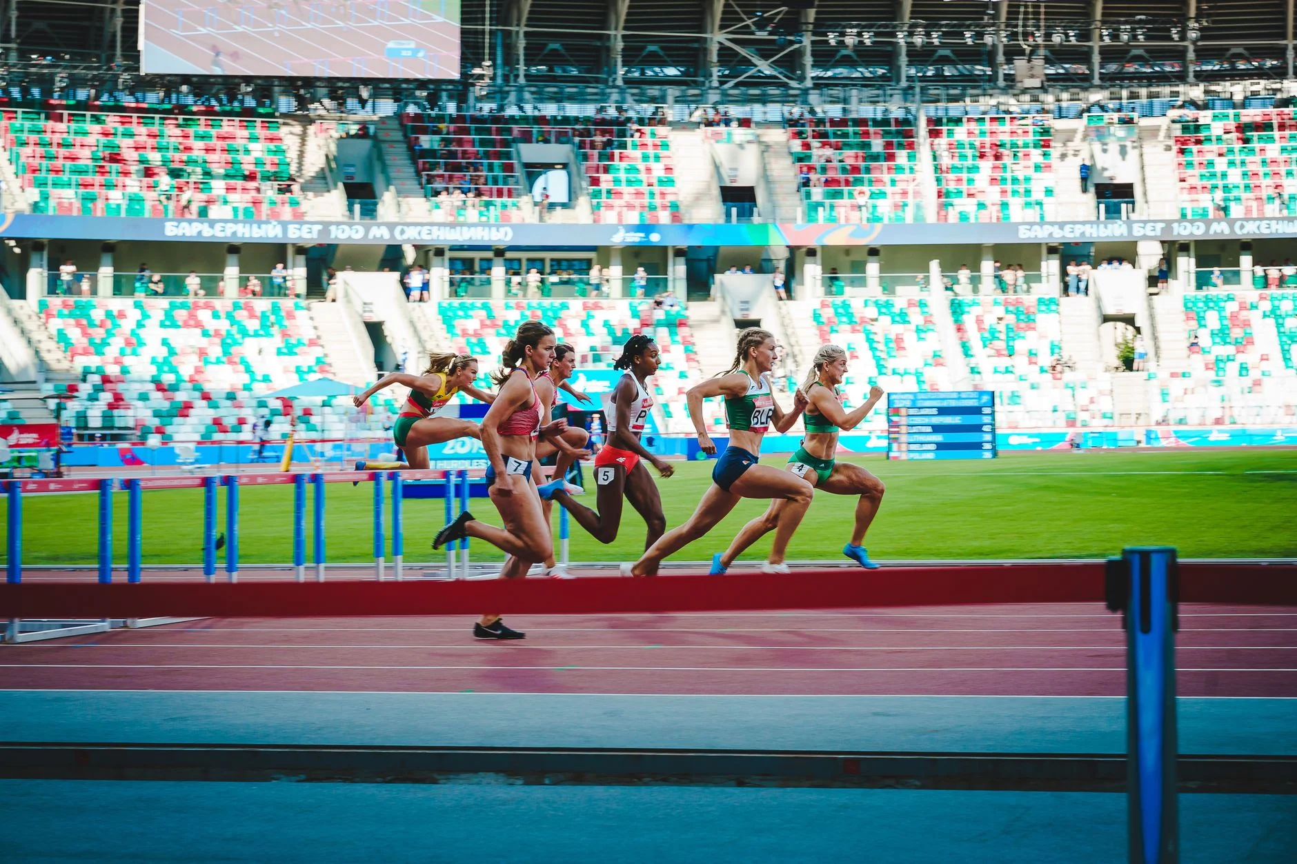 Women sprinting over hurdles on a track in front of a full stadium