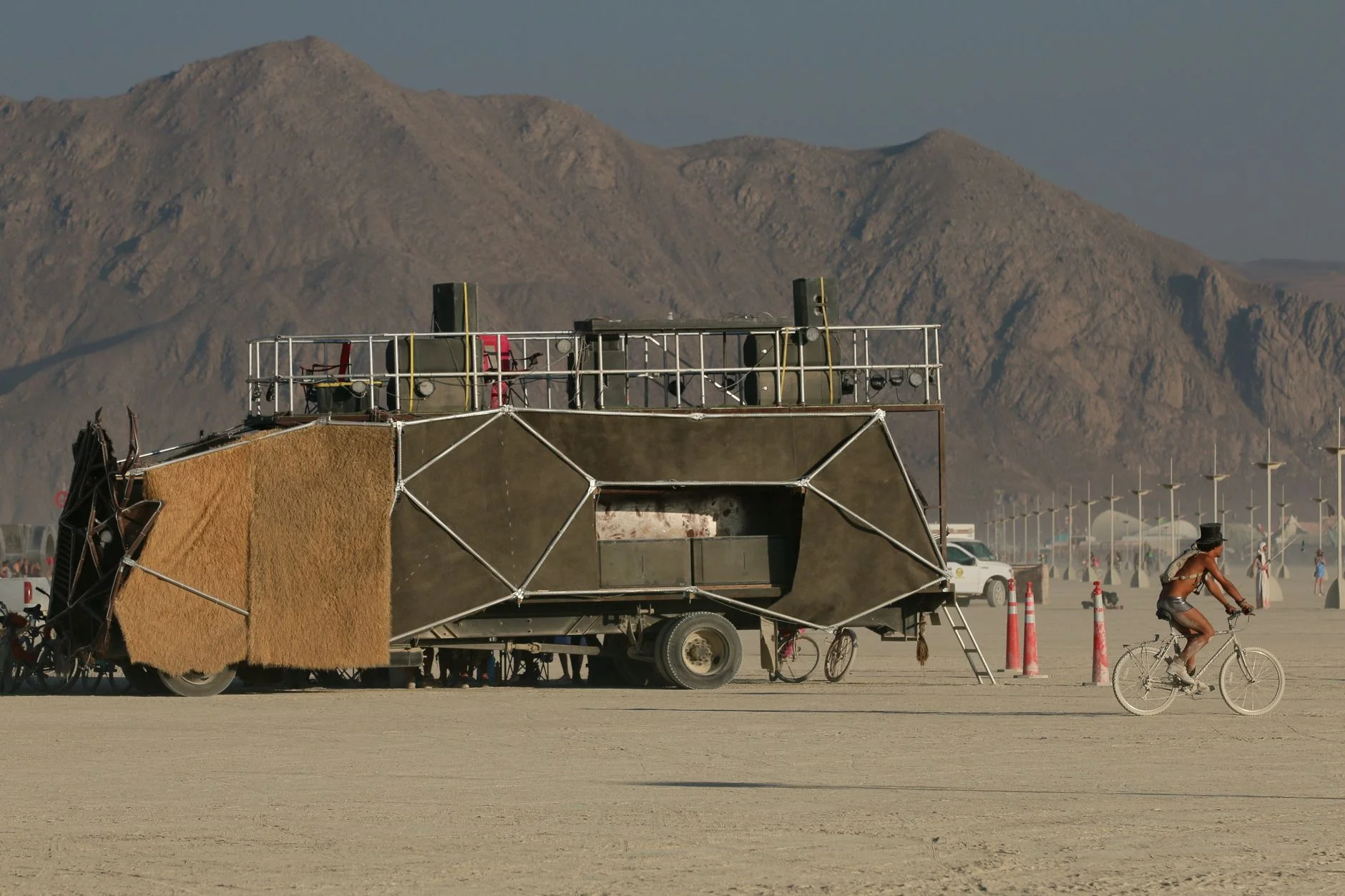 A creative art car in the desert with a cyclist riding nearby