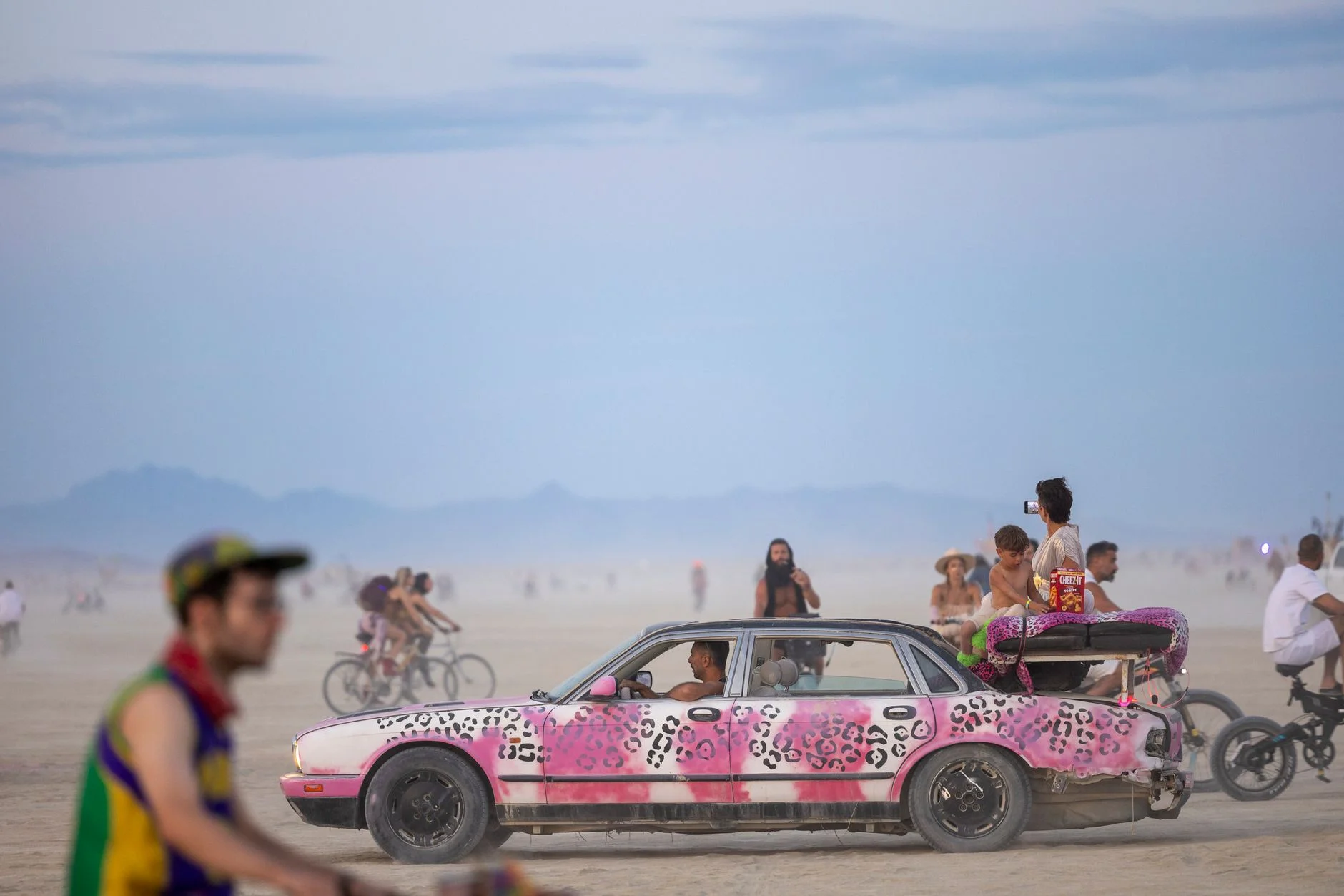 A colorful art car and cyclists riding through a desert arts festival