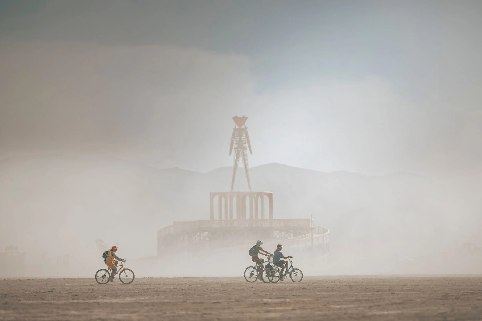 Cyclists riding through dust near a desert festival effigy