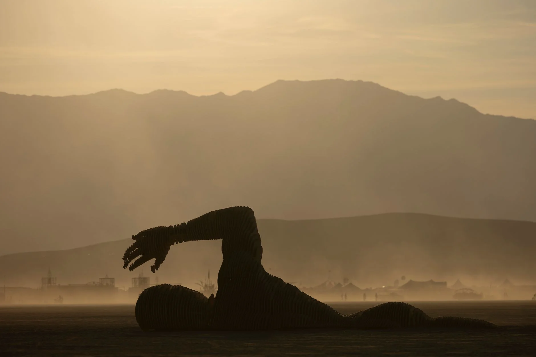 Silhouette of a giant sculpture against a mountain backdrop at dusty desert sunset