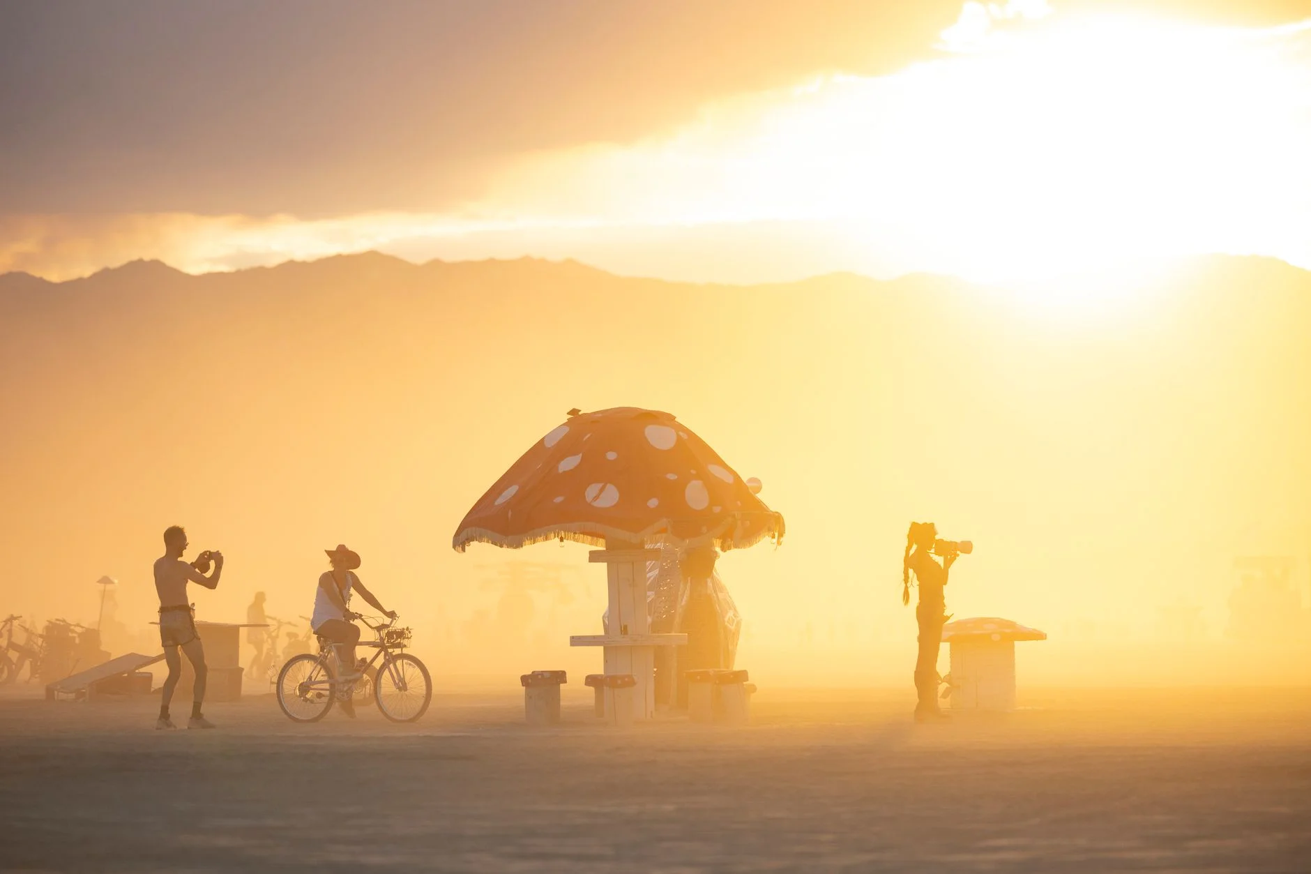 Silhouettes of festivalgoers enjoying sunset near a whimsical sculpture at a desert arts festival