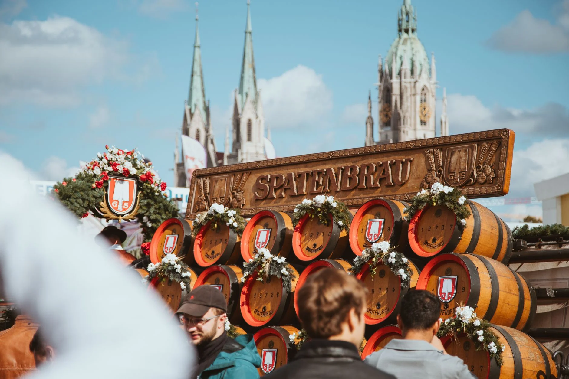 A festive Oktoberfest beer tent scene with barrels and celebrating crowds under a clear sky
