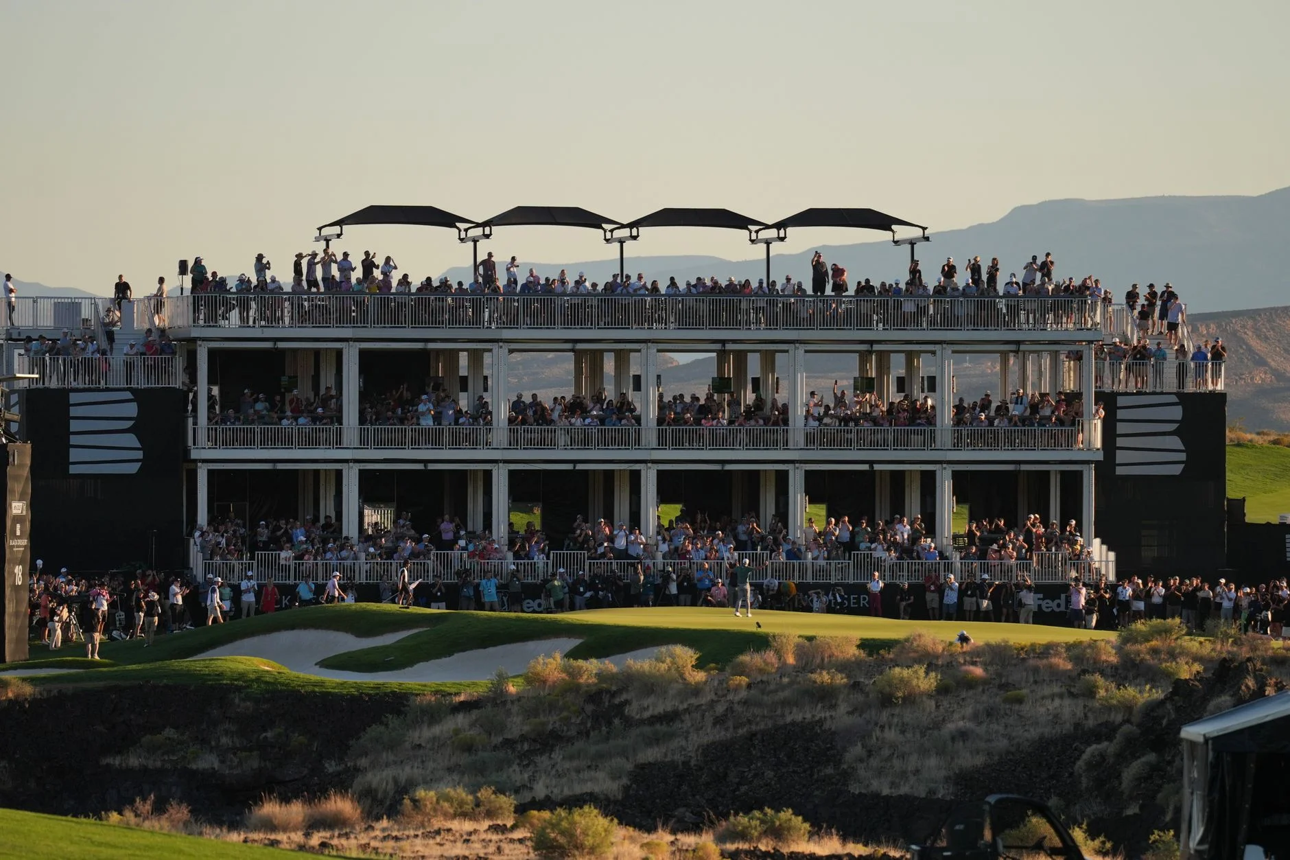 A crowd of spectators gathered at a golf tournament viewing structure at dusk