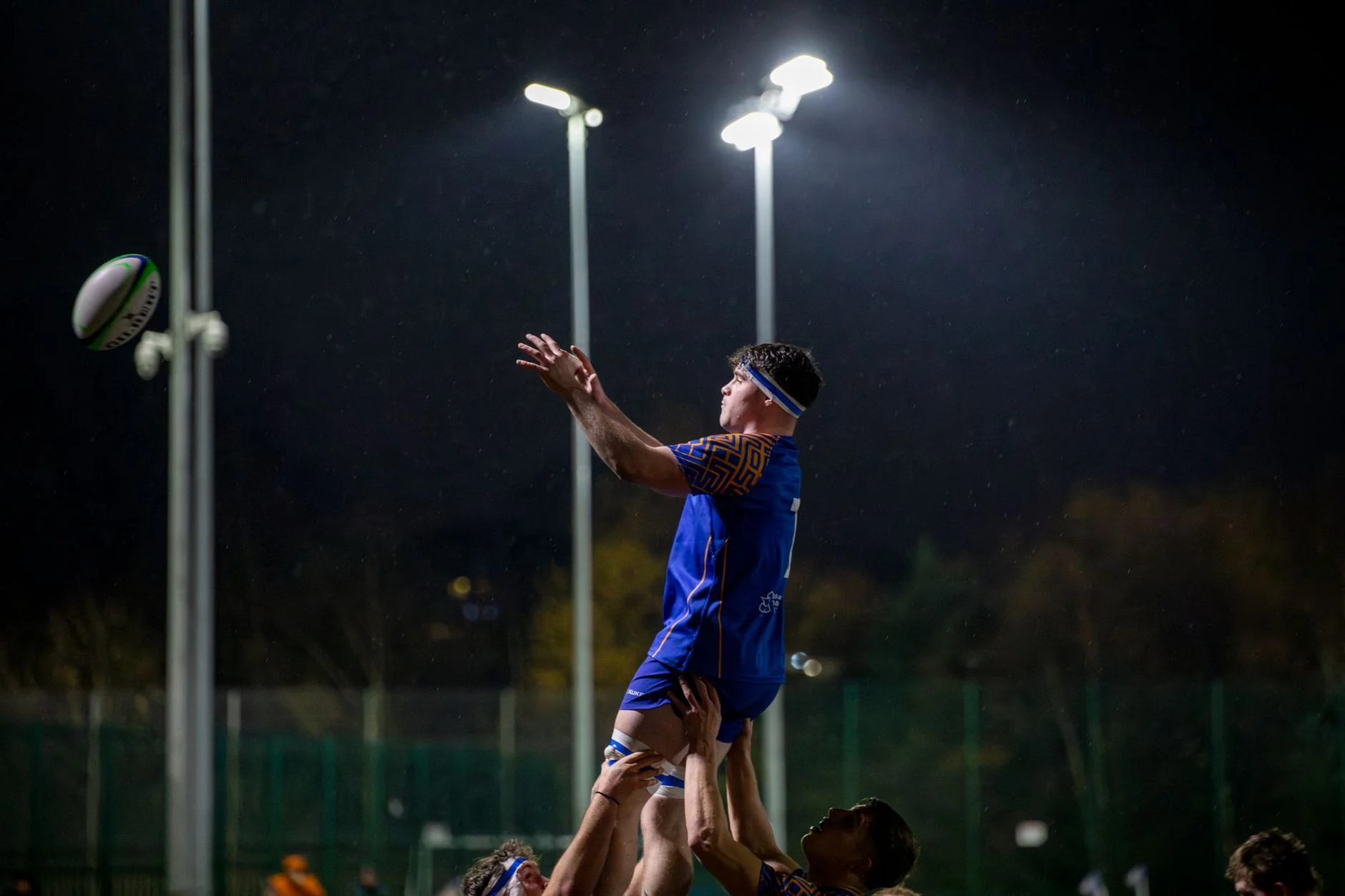 A rugby player catching the ball during a floodlit night match