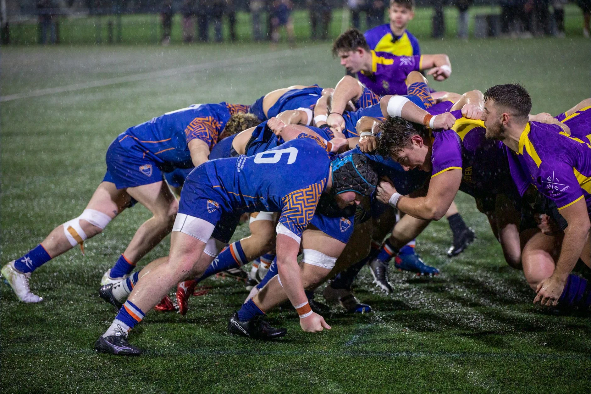 Two rugby teams packing into a scrum on a grass field