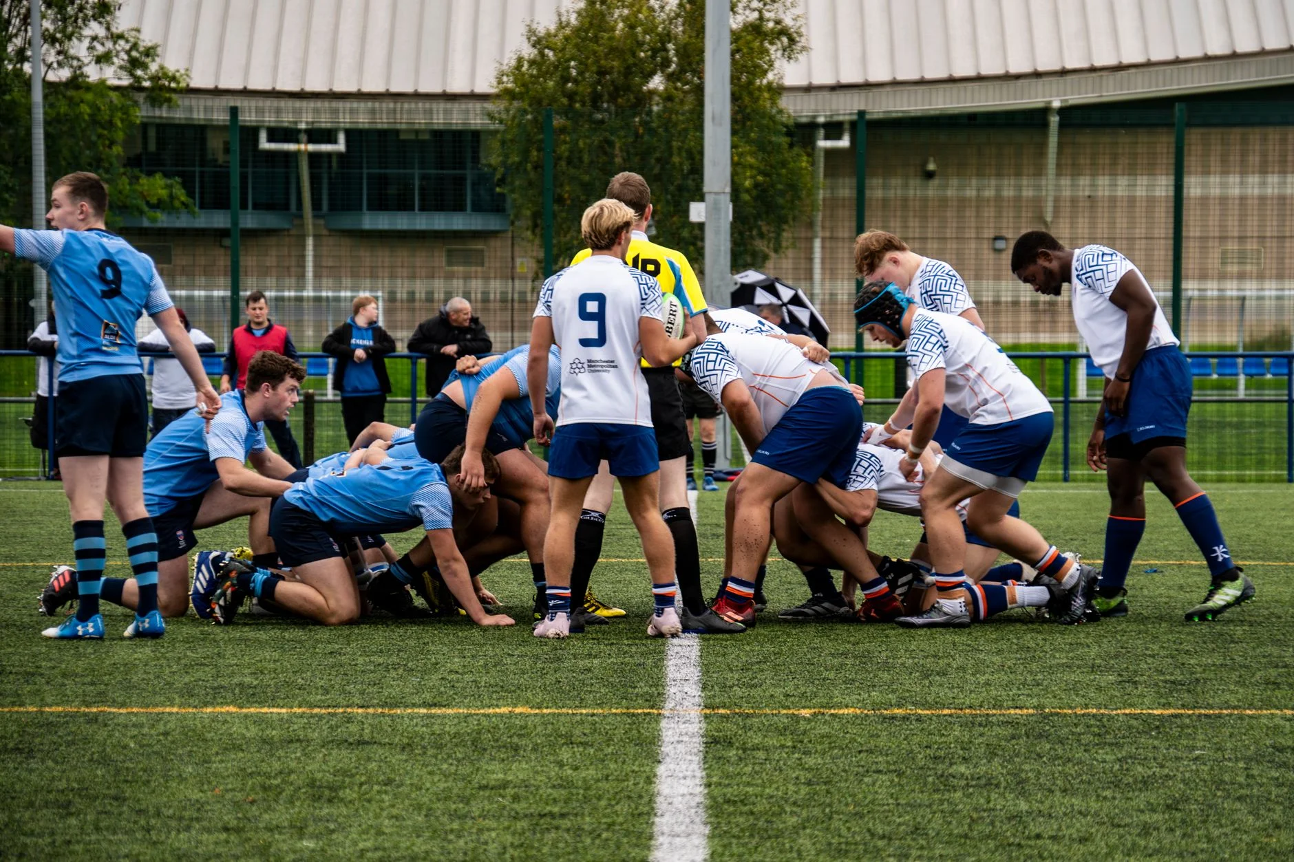 Two rugby teams facing off across the ball on a grass pitch