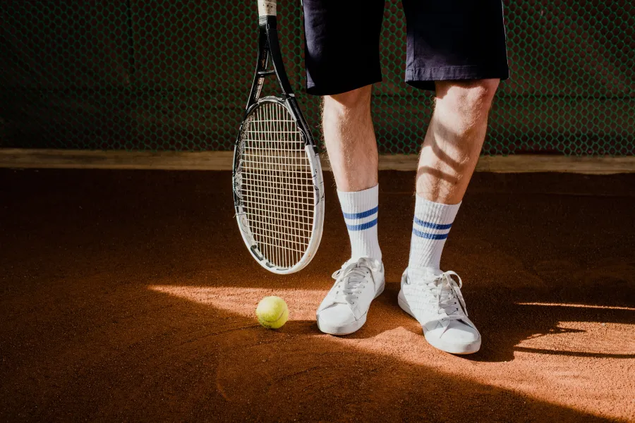 A player's feet beside a tennis ball on a sunlit clay court