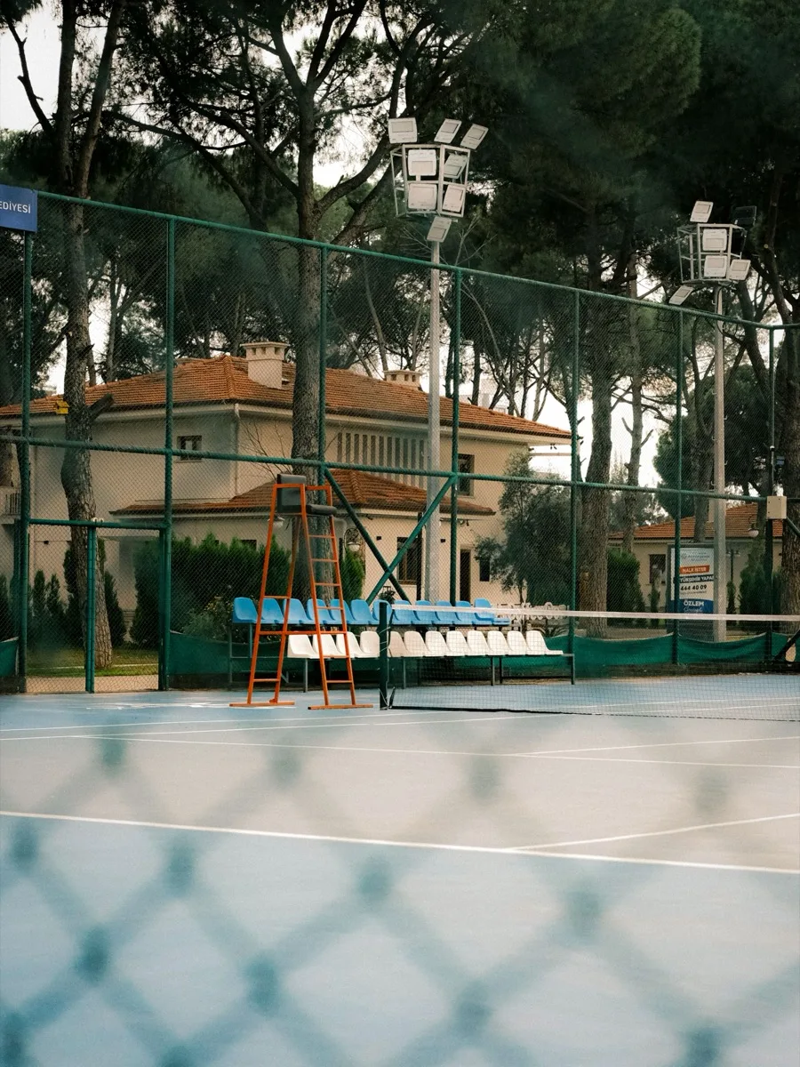 A tennis court with a clubhouse behind it, viewed through the court fence